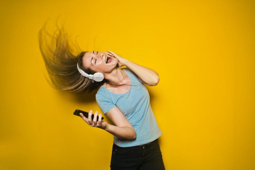 jeune femme écoutant un contenu dans un casque audio et dansant devant un mur jaune